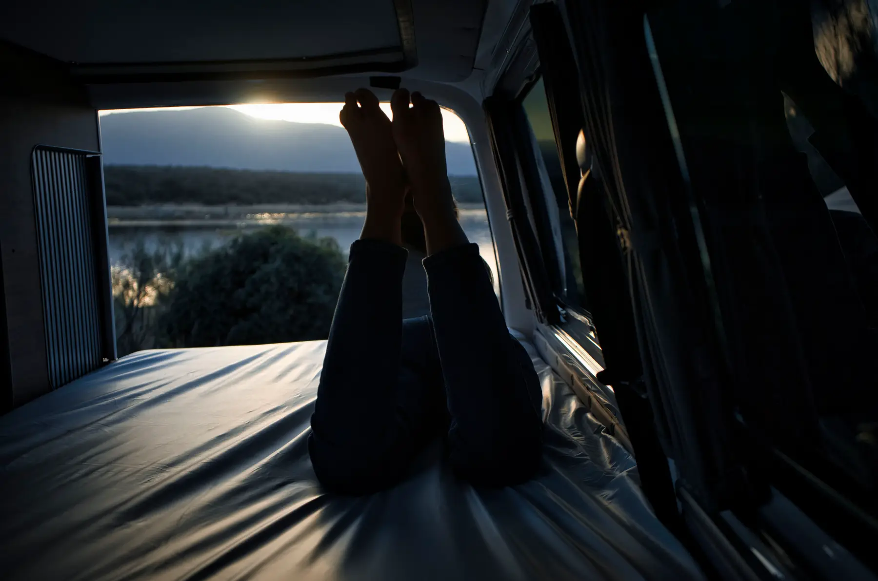 Interior de camper beWinkle al atardecer con vistas a un embalse desde la cama